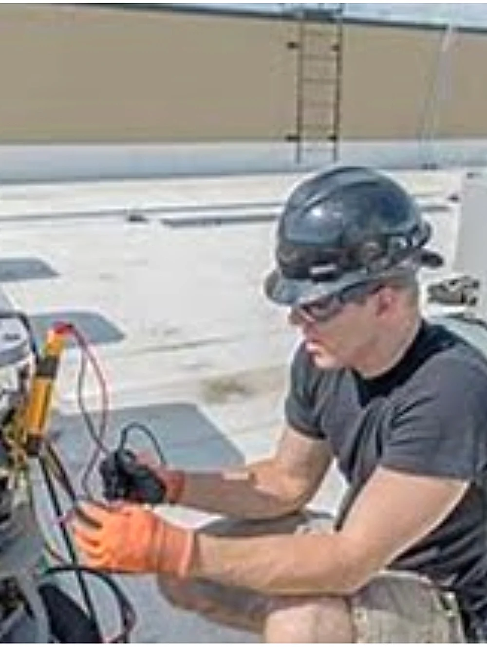 Technician in a hard hat checking refrigerant pressure with gauges on a rooftop condensing unit